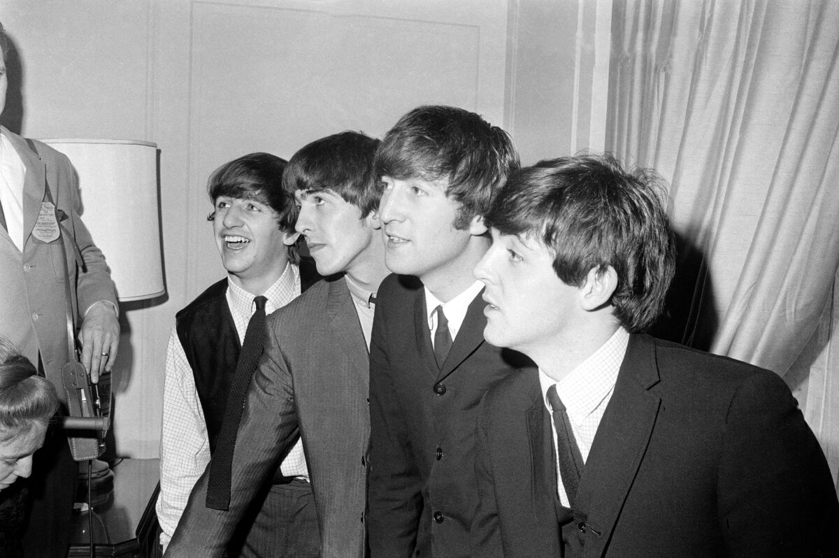 A black-and-white photo of four young men in suits with floppy hair.