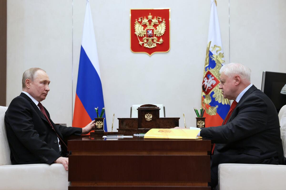 Vladimir Putin and Sergey Mironov sit across from each other at a desk with flags in the background