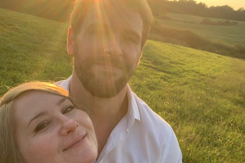 A man and a woman pose for a selfie in a park with the sun beaming behind them.