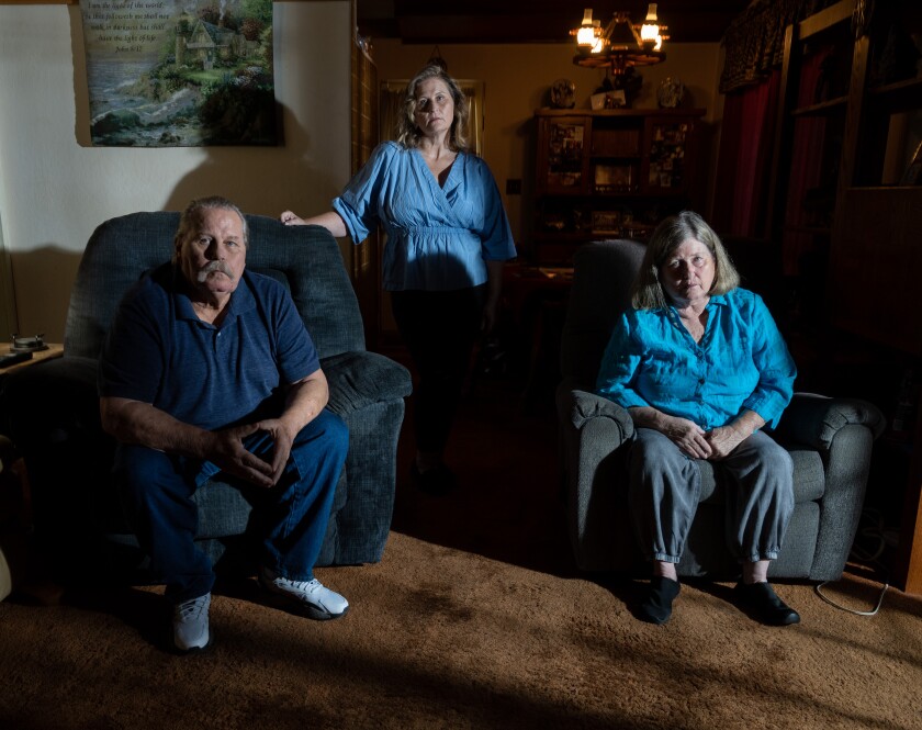 Brandi Michalik stands and her parents, Ray and Connie Michalik. sit in chairs in front of her in a room.