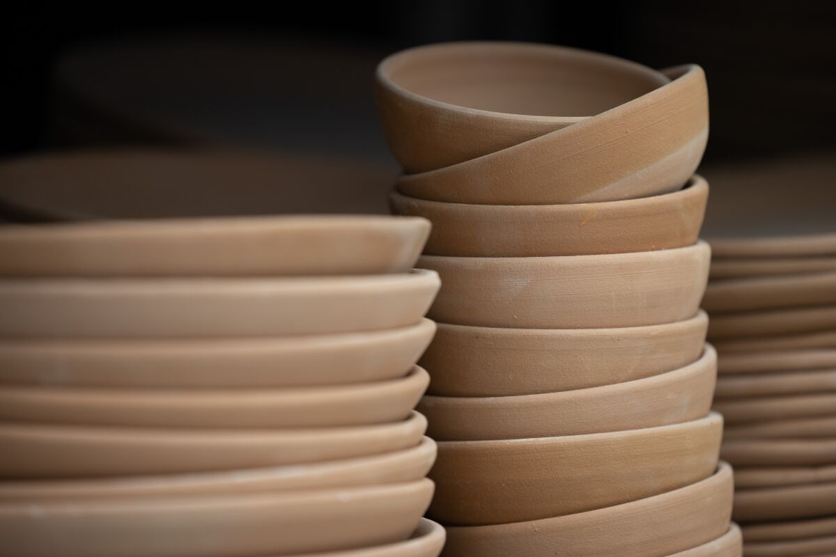 Plates and bowls await finishing glaze, stacked on a shelf at The Wheel Stoneware. All of the wares in the shop are handmade.