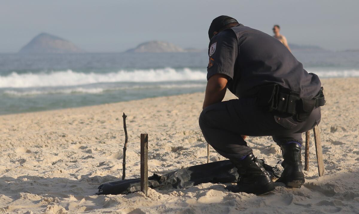 A police officer bends over human remains, covered in a plastic bag, discovered on Copacabana Beach near the Olympic beach volleyball venue on Wednesday.