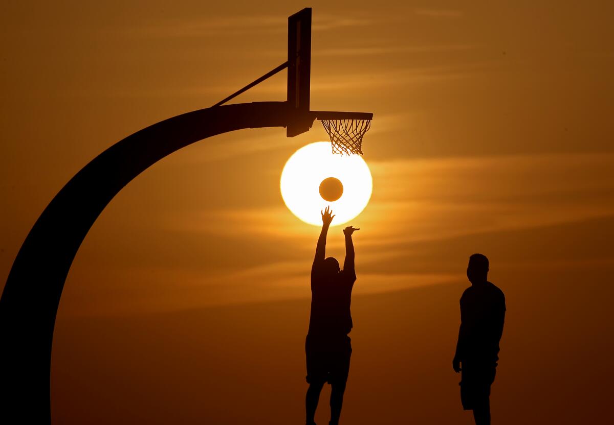 Two people play basketball, silhouetted by the setting sun