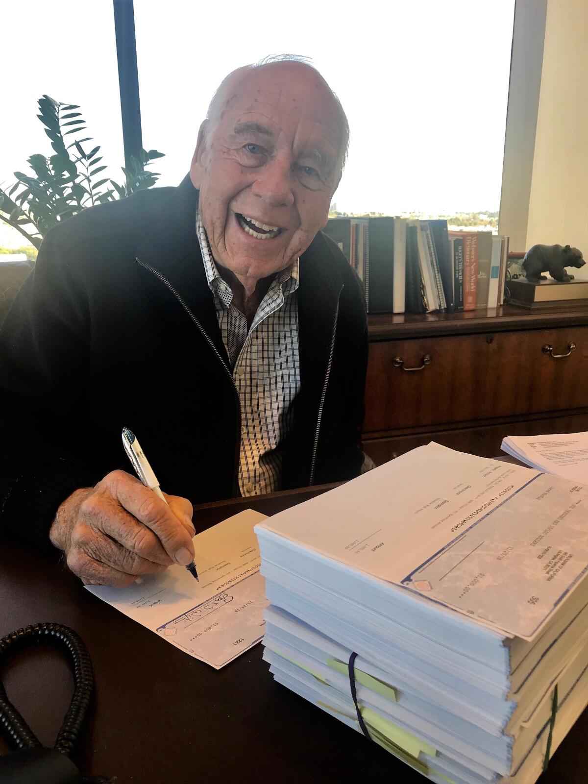 Bob Wilson hand-signing more than 1,000 checks for $1,000 to Paradise High students and staff