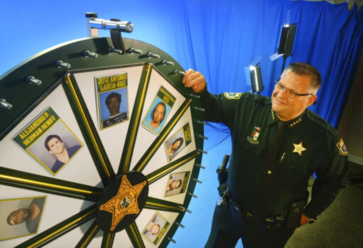 In this July 2017 photo, Brevard County Sheriff Wayne Ivey gets ready to spin his popular "Wheel of Fugitive" in Titusville, Fla. The popular videos feature photos of 10 of the county's most wanted criminals. (Malcolm Denemark/Florida Today via AP)