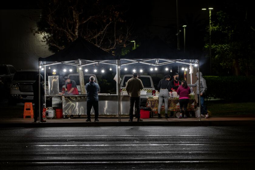 SANTA ANA, CA - DECEMBER 27, 2022: Customers wait in line on a rain slicked evening for warm food from a street vendor on the sidewalk off McFadden Avenue on December 27, 2022 in Santa Ana, California.The City of Santa Ana is cracking down on unlicensed street vendors in the city. In the past two months, the city has shut down 100 of the businesses temporarily. The businesses were back up within a few days moving to different locations. (Gina Ferazzi / Los Angeles Times)