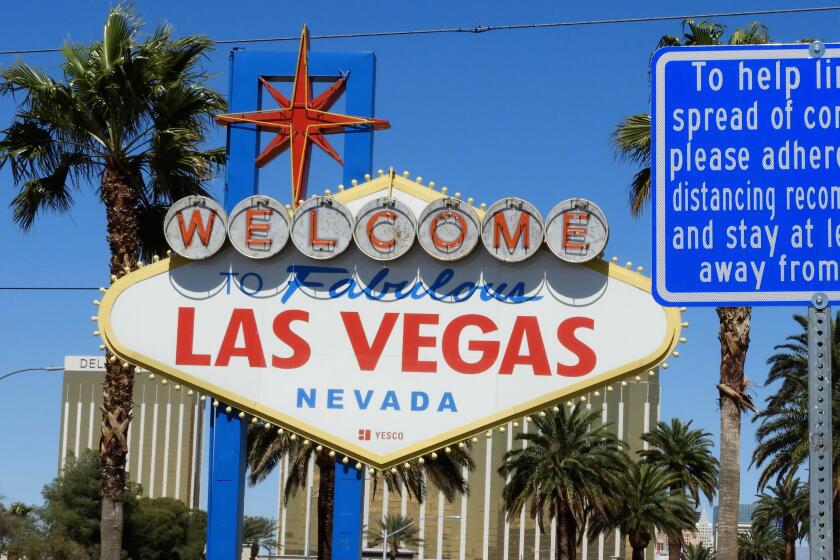 A large, white sign that reads "Welcome to fabulous Las Vegas Nevada," next to a blue sign with COVID-19 guidelines