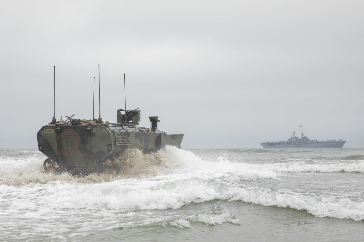 An Amphibious Combat Vehicle drives into the ocean with amphibious assault ship Makin Island in distance.