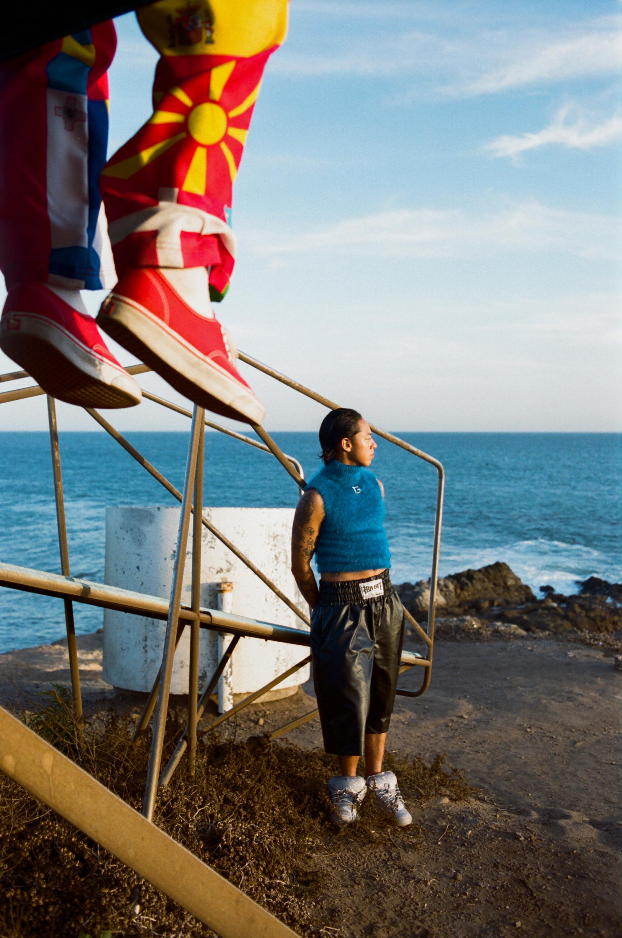 A person wearing a blue top and black pants looks out into the ocean. 