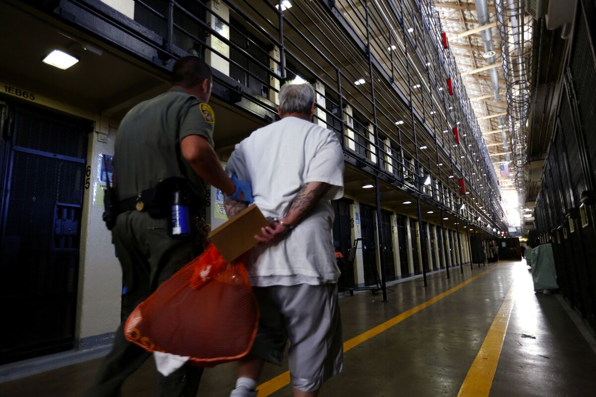 A man in handcuffs is escorted by a uniformed officer past inmate cells