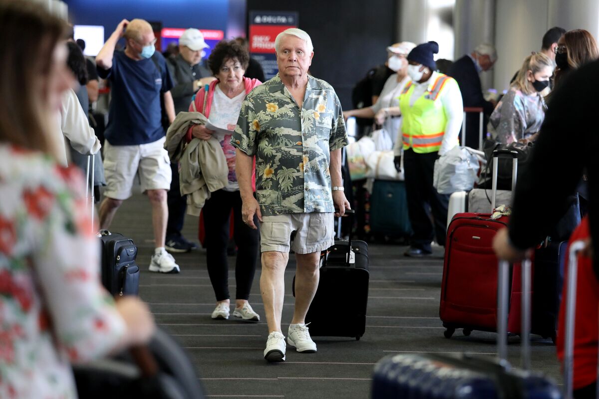 Passengers, some masked and others not, walk through a terminal at LAX.