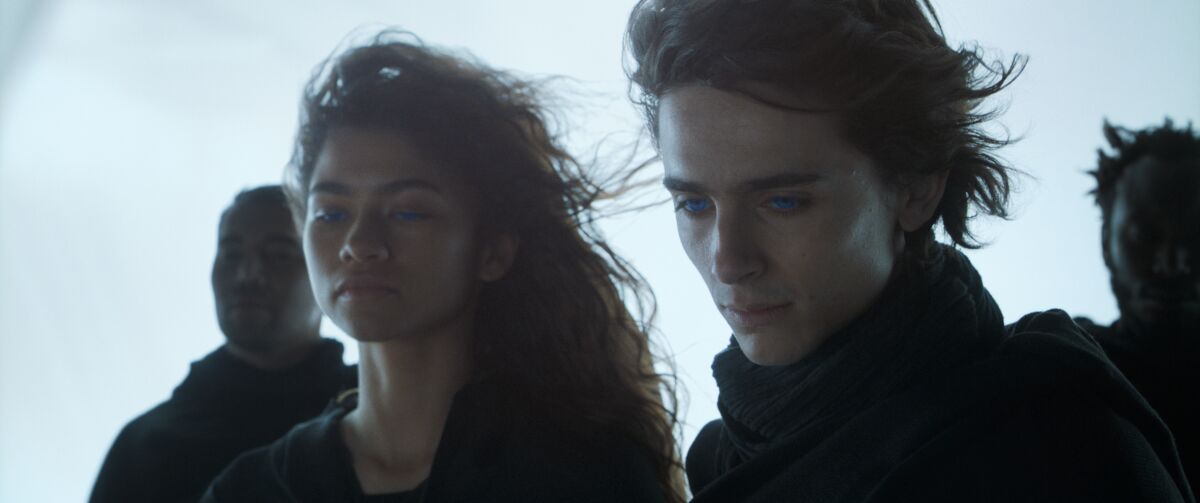 Zendaya stands next to Timothee Chalamet, both looking downward and sad, in a scene from "Dune." 
