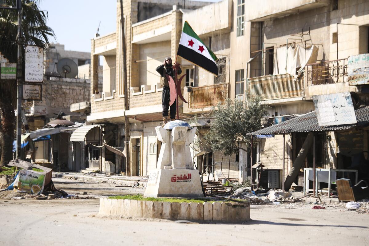 A man stands on a statue holding a Syrian flag in Saraqeb, Syria.