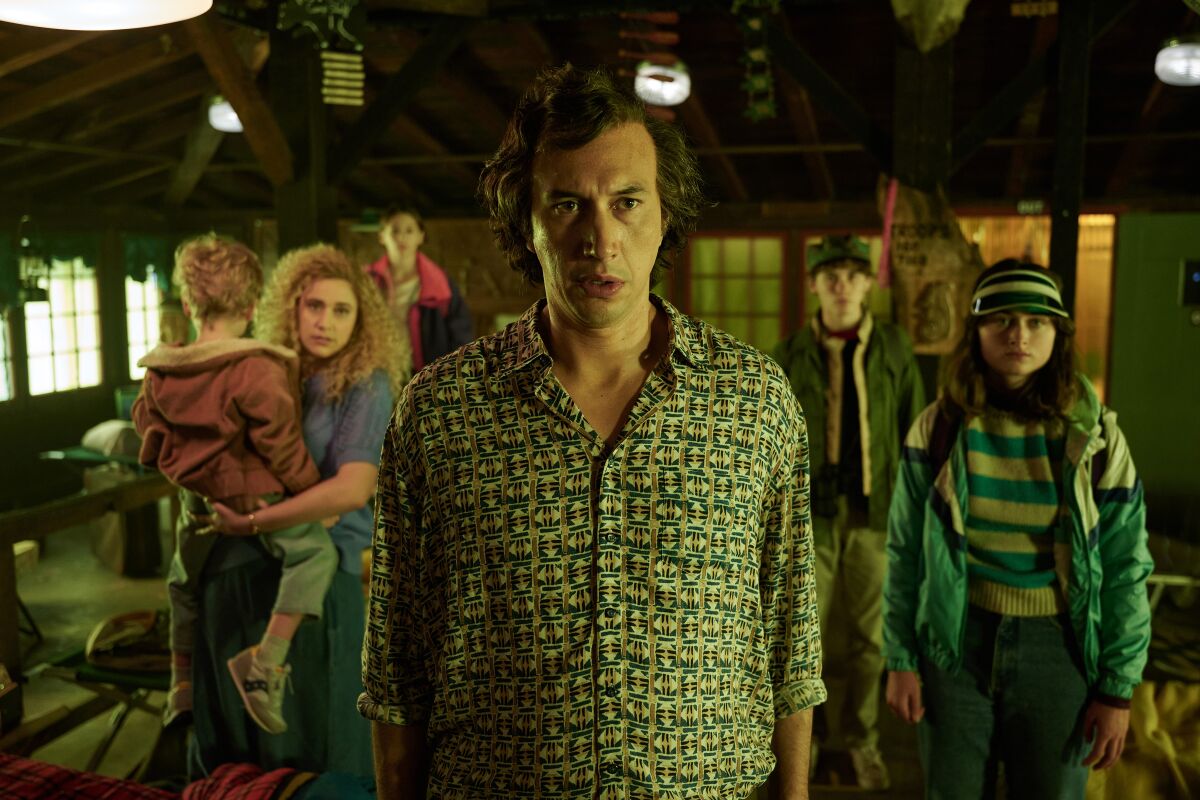 A man in a green pattern shirt with a woman holding a child and three older children behind him in the movie "White Noise."
