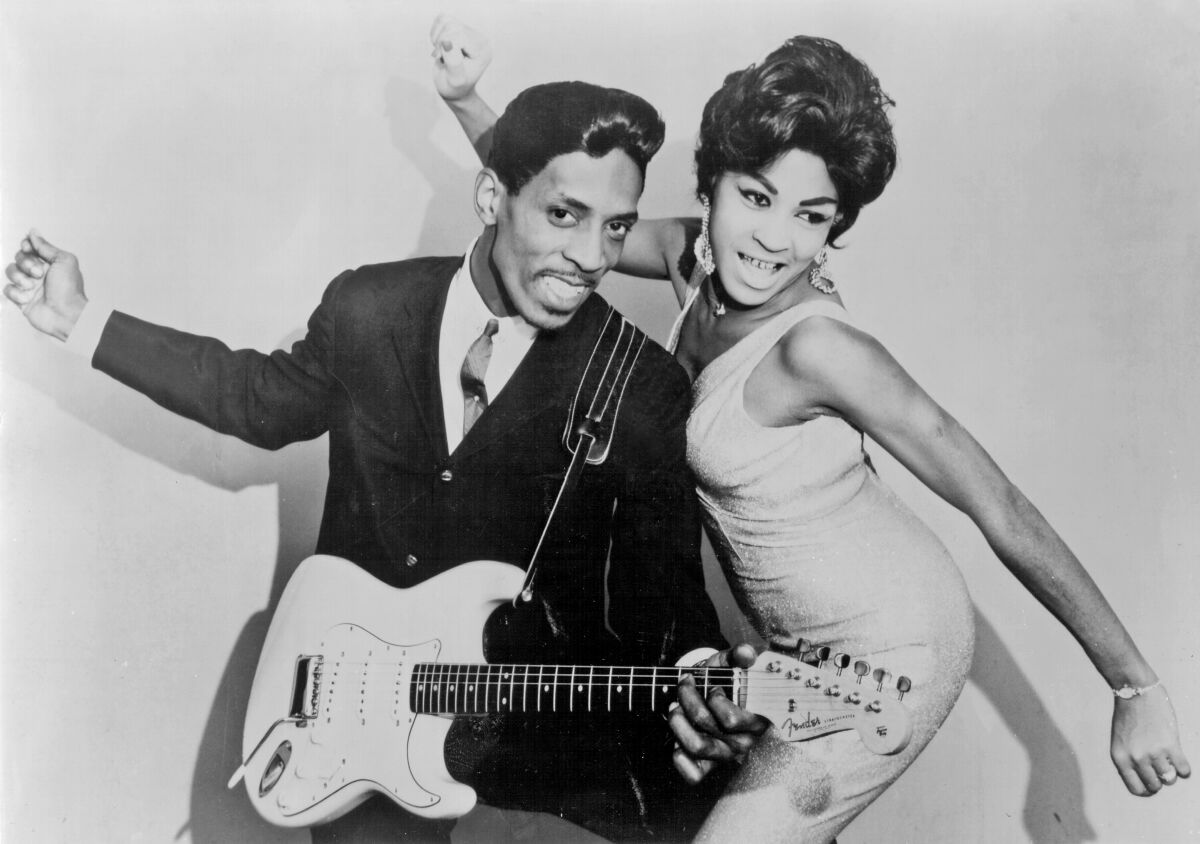 A black-and-white portrait of Ike and Tina Turner posing for a picture, singing and dancing. 