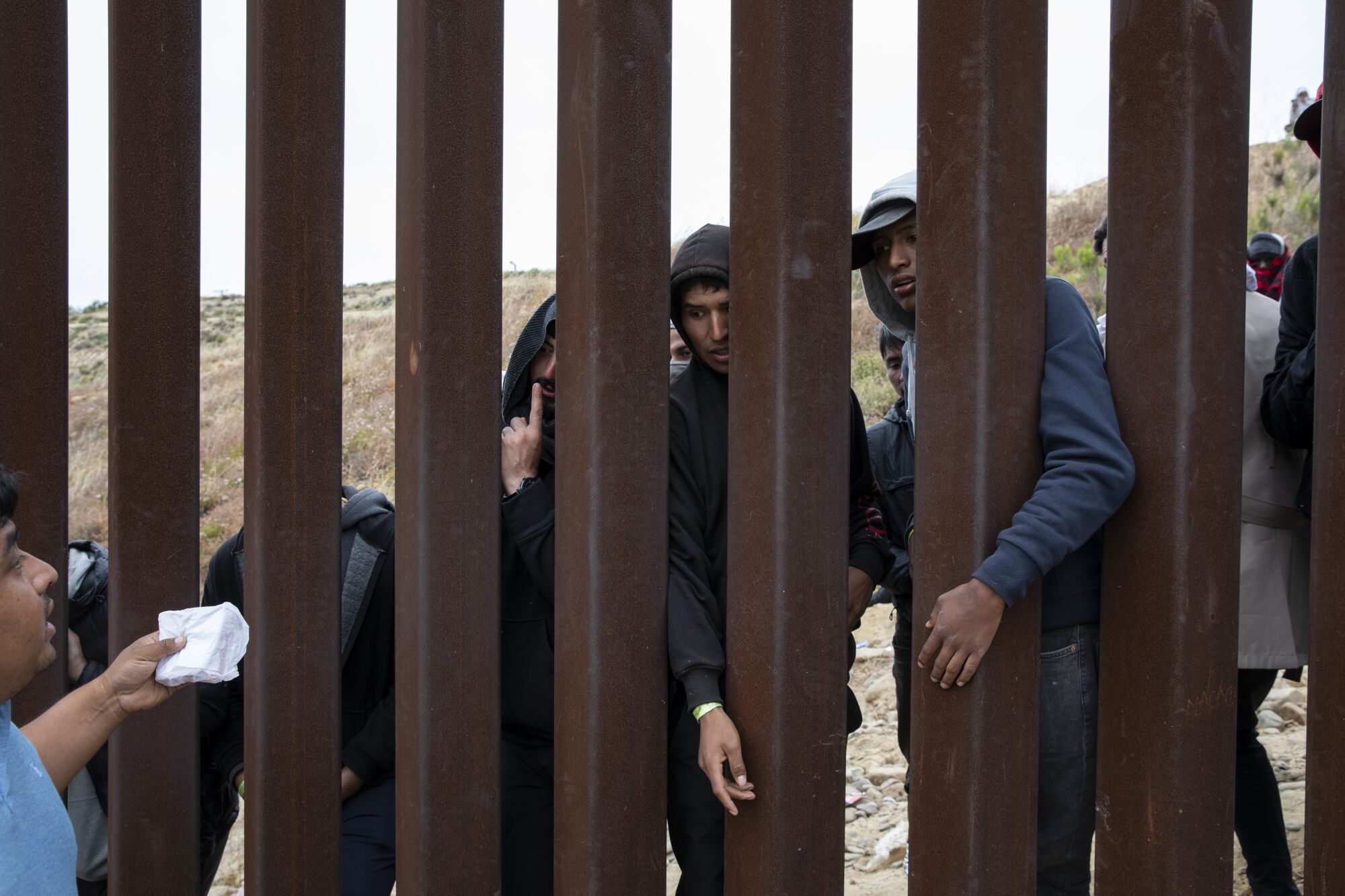 A group of men buy food and phone chargers as they wait between the border walls that separate Tijuana from San Diego.