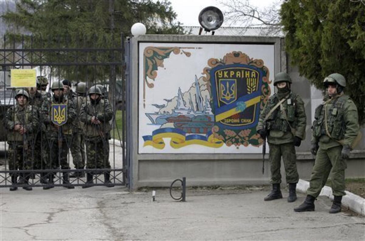 Ukrainian soldiers, left, and unidentified gunmen gather at the gate of an infantry base in Privolnoye, in the Crimean region. Hundreds of the unidentified gunmen have arrived outside the base with vehicles that bear Russian license plates. The vehicles have surrounded the base and reportedly are blocking Ukrainian soldiers from entering or leaving.