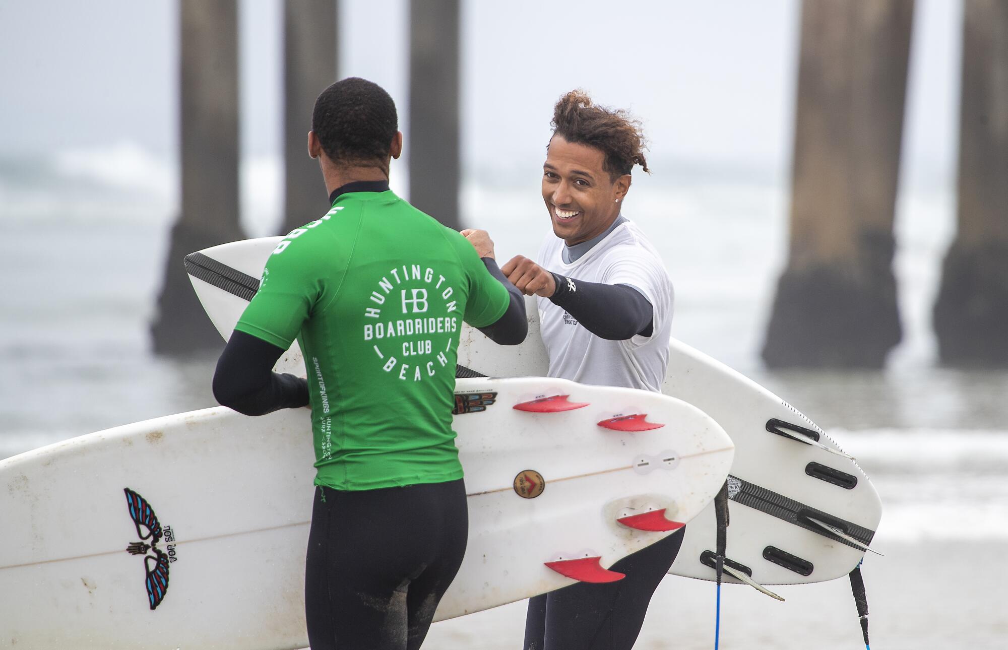 Two surfers fist-bump as they walk to the water.