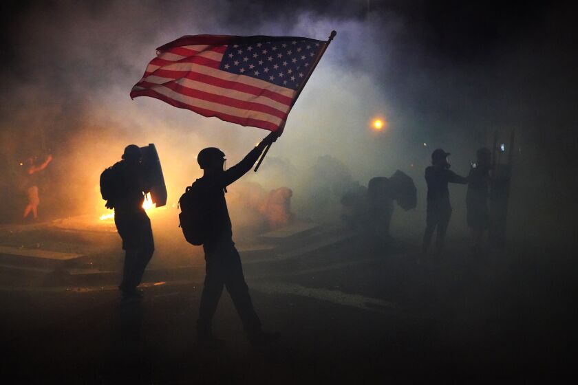 PORTLAND, OR - JULY 21: A protester flies an American flag while walking through tear gas fired by federal officers during a protest in front of the Mark O. Hatfield U.S. Courthouse on July 21, 2020 in Portland, Ore. The federal police response to the ongoing protests against racial inequality has been criticized by city and state elected officials. (Photo by Nathan Howard/Getty Images)