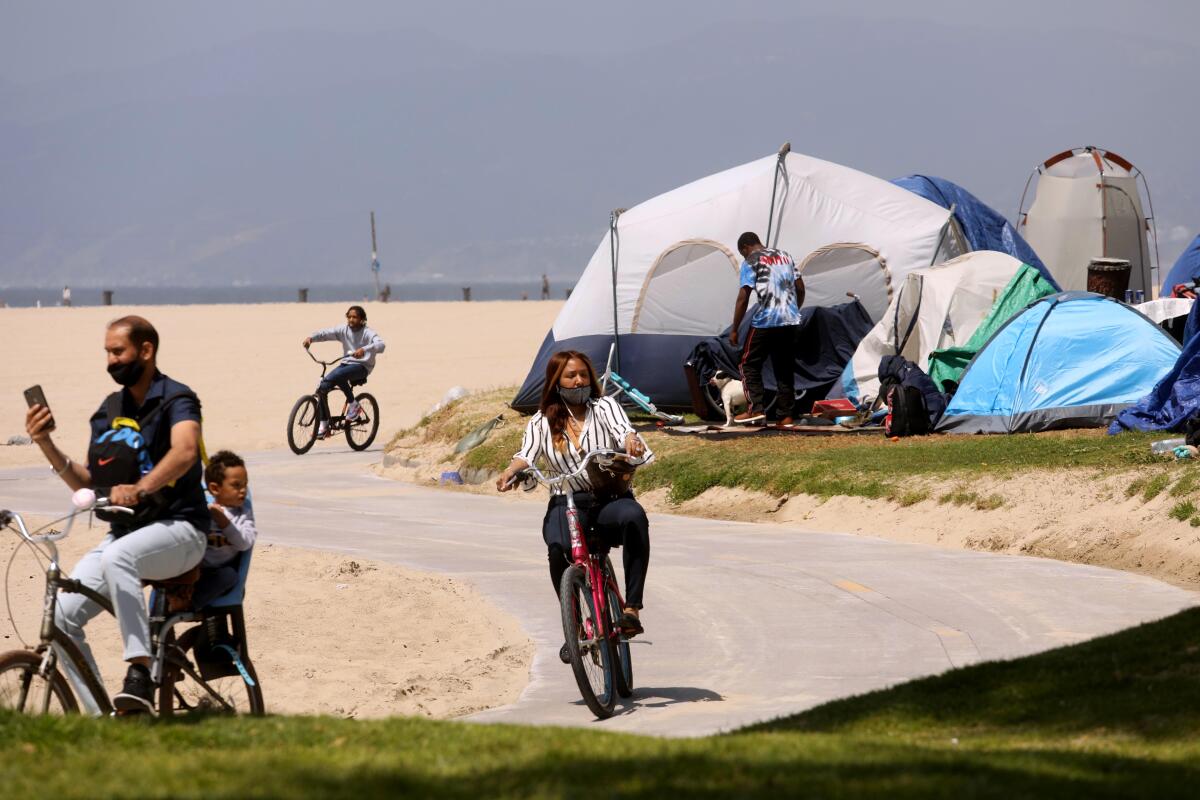 Bicyclists ride past several tents along the beach