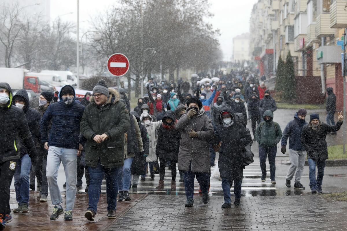 A crowd of demonstrators in winter gear, some wearing face masks, march on a brick walkway in Minsk, Belarus