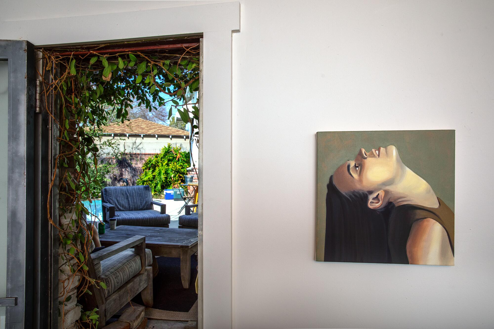 An oil painting of a woman hangs on a wall next to an open door that leads to a backyard with pool
