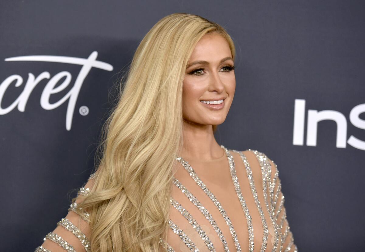 Paris Hilton smiling in a striped silver and nude dress