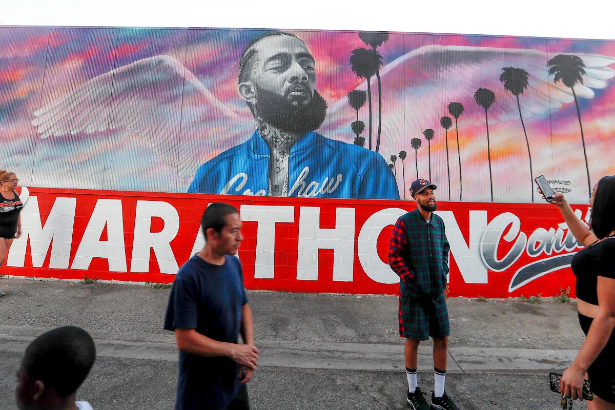 Visitors take photos and videos near a mural of Nipsey Hussle.