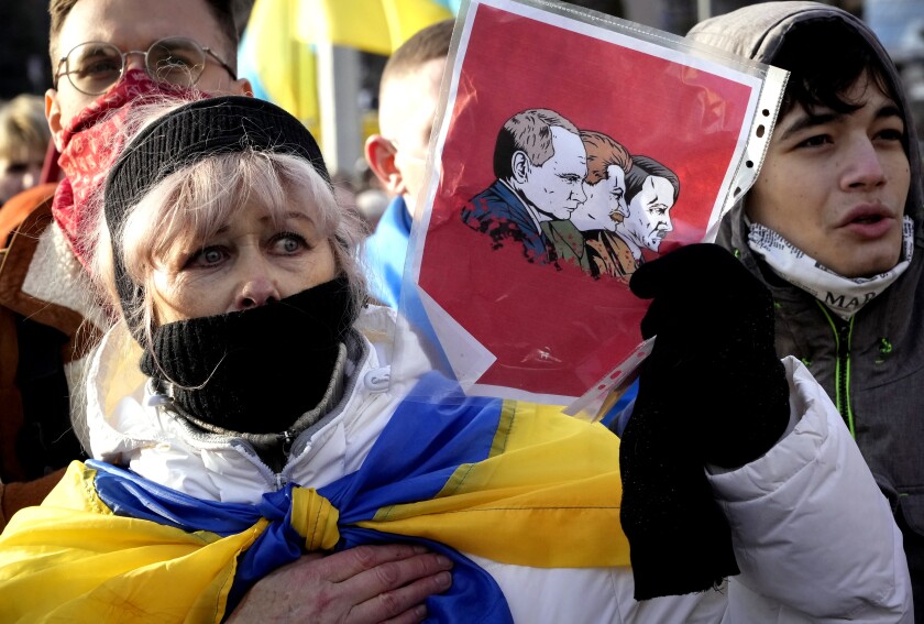 A woman holds a drawing of Putin with Stalin and Hitler at a protest.