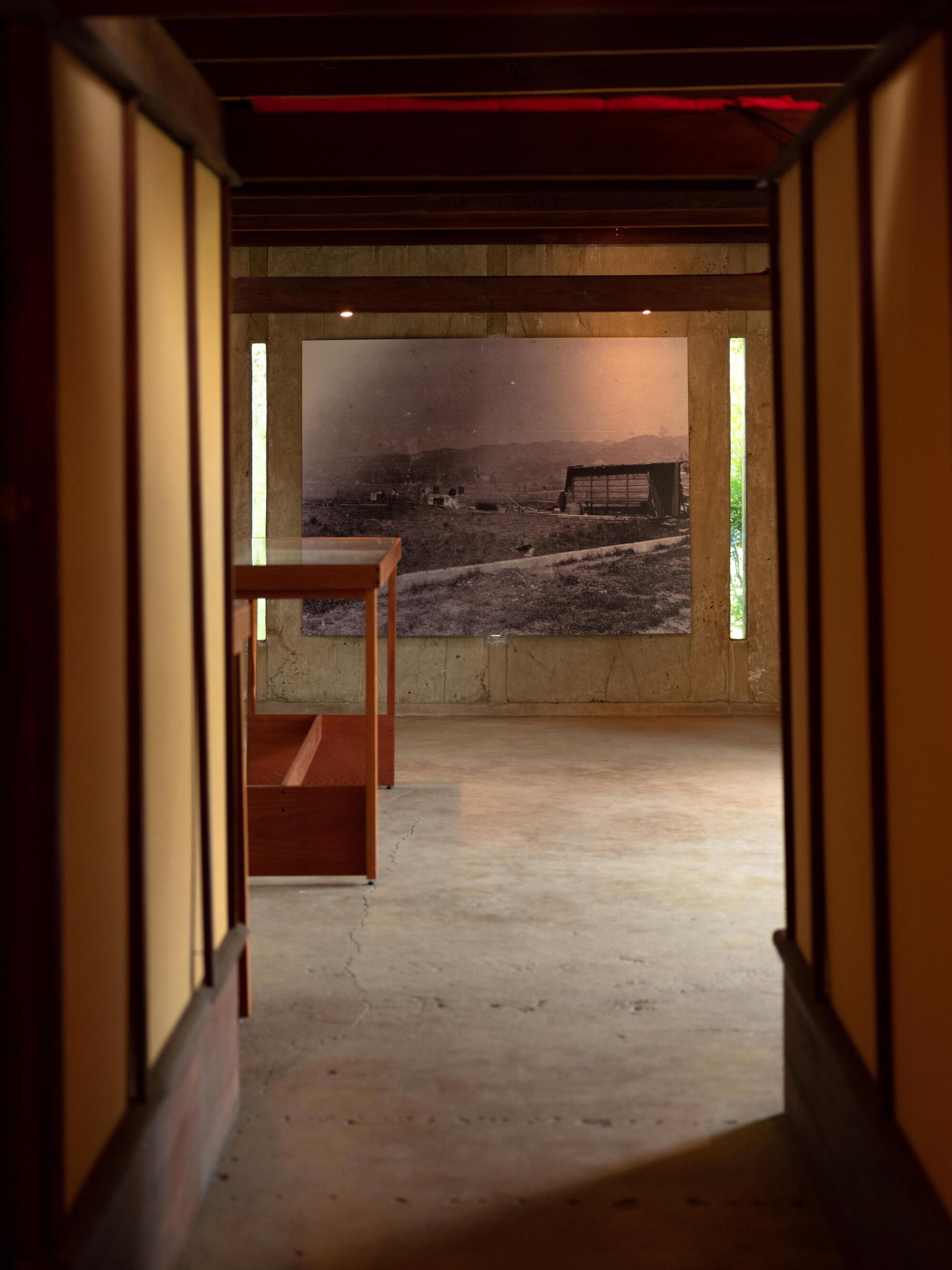 A view through a wood-lined hallway ends on a room where a vintage photograph is displayed on a concrete wall.