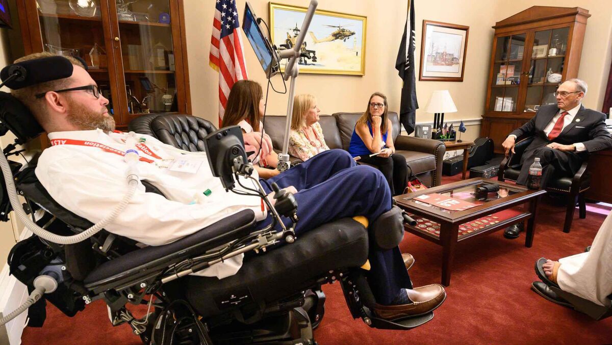 A group of people, one in a wheelchair, sit in a congressman's office.