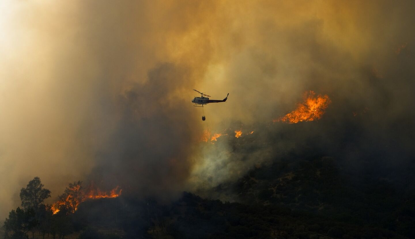 A water-dropping helicopter flies through thick smoke and active flame.