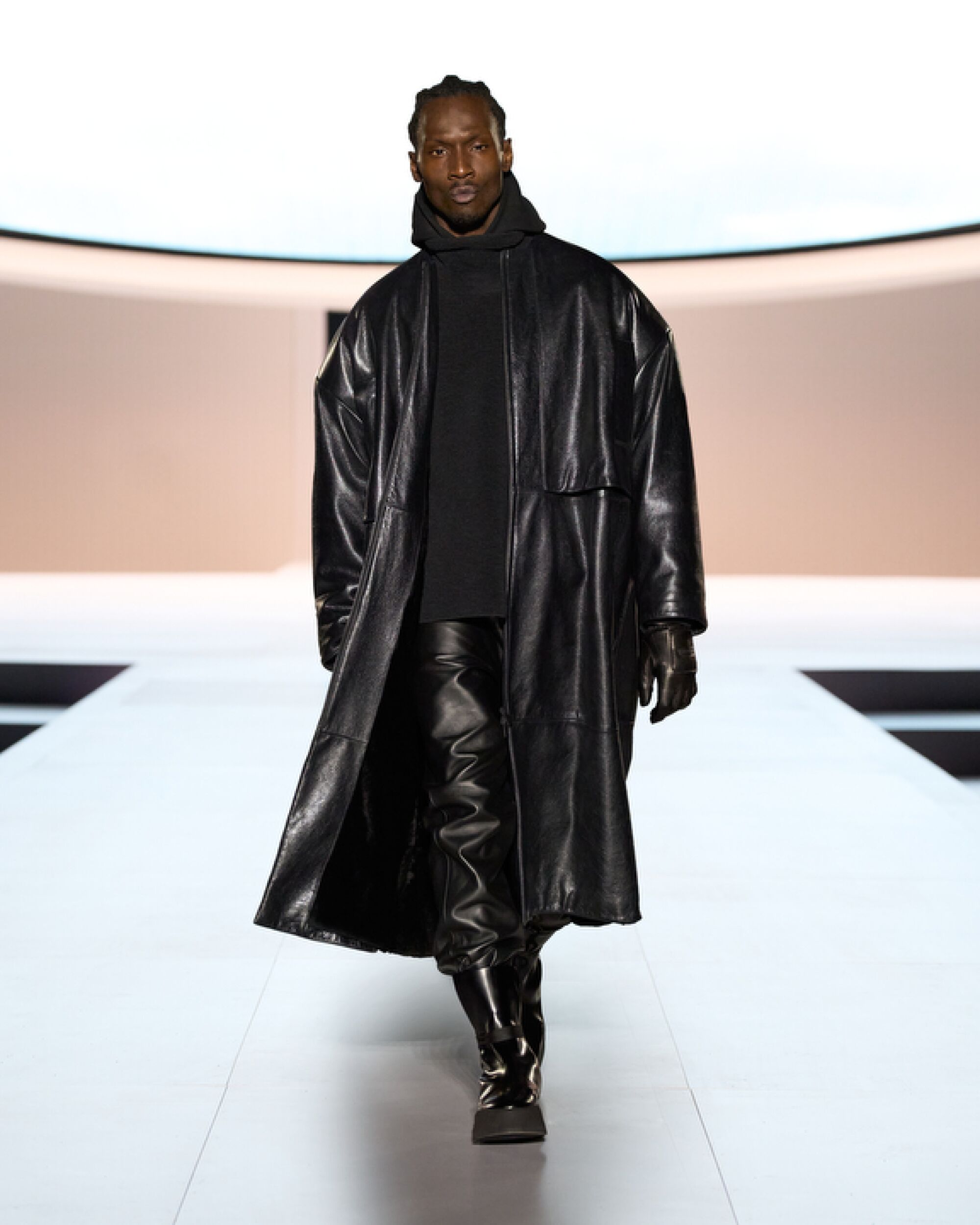 Model wears black leather outfit on runway.