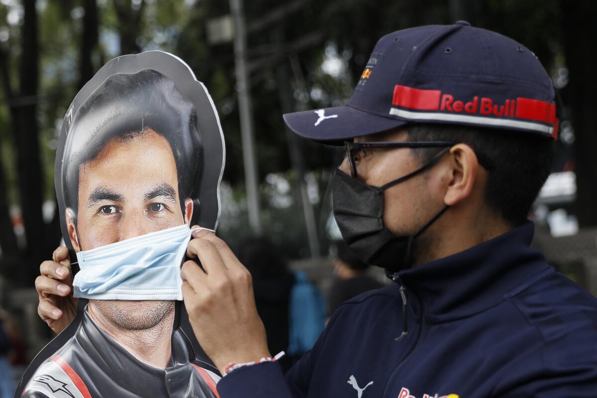 A man adjusts a face mask on a promotional cardboard cutout of Sergio "Checo" Pere 