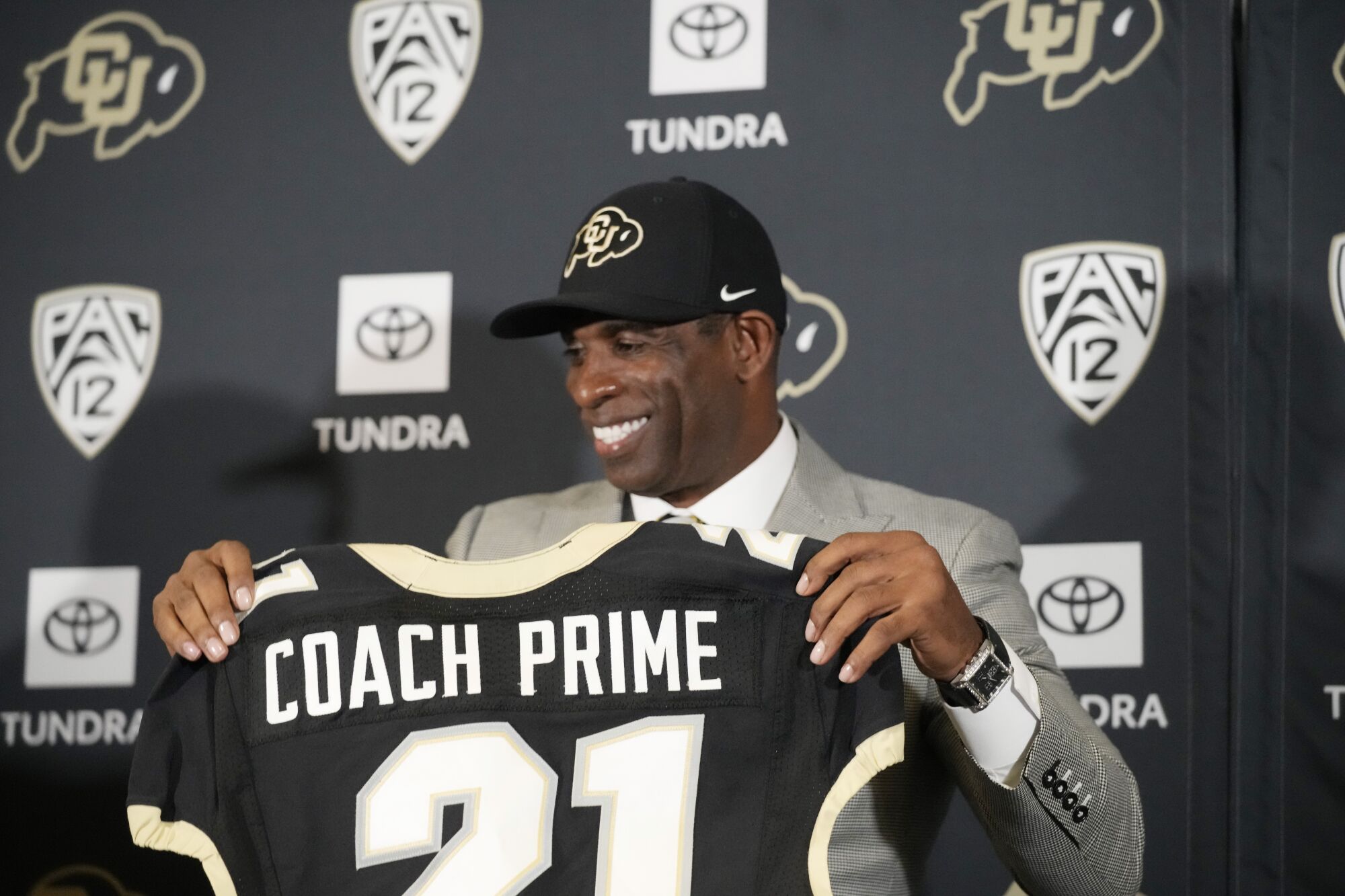 Deion Sanders holding a jersey with 'Coach Prime' on it after being introduced as Colorado's new coach 