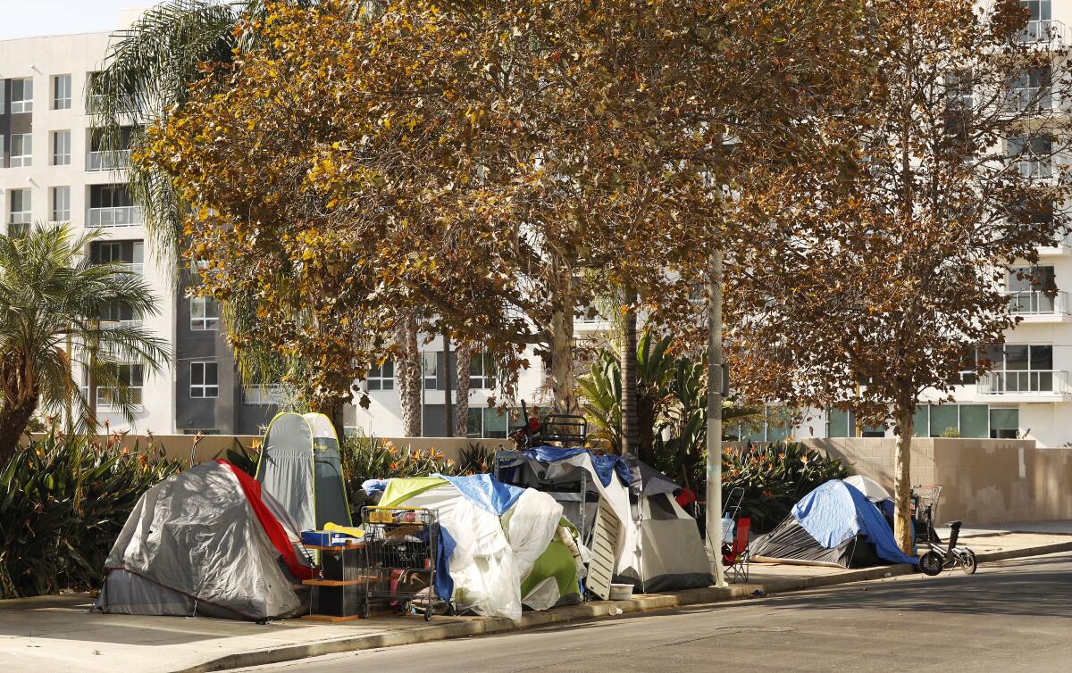 Tents on a city sidewalk with a large apartment building in the background
