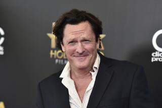 Michael Madsen smiles in a black blazer and white patterned shirt