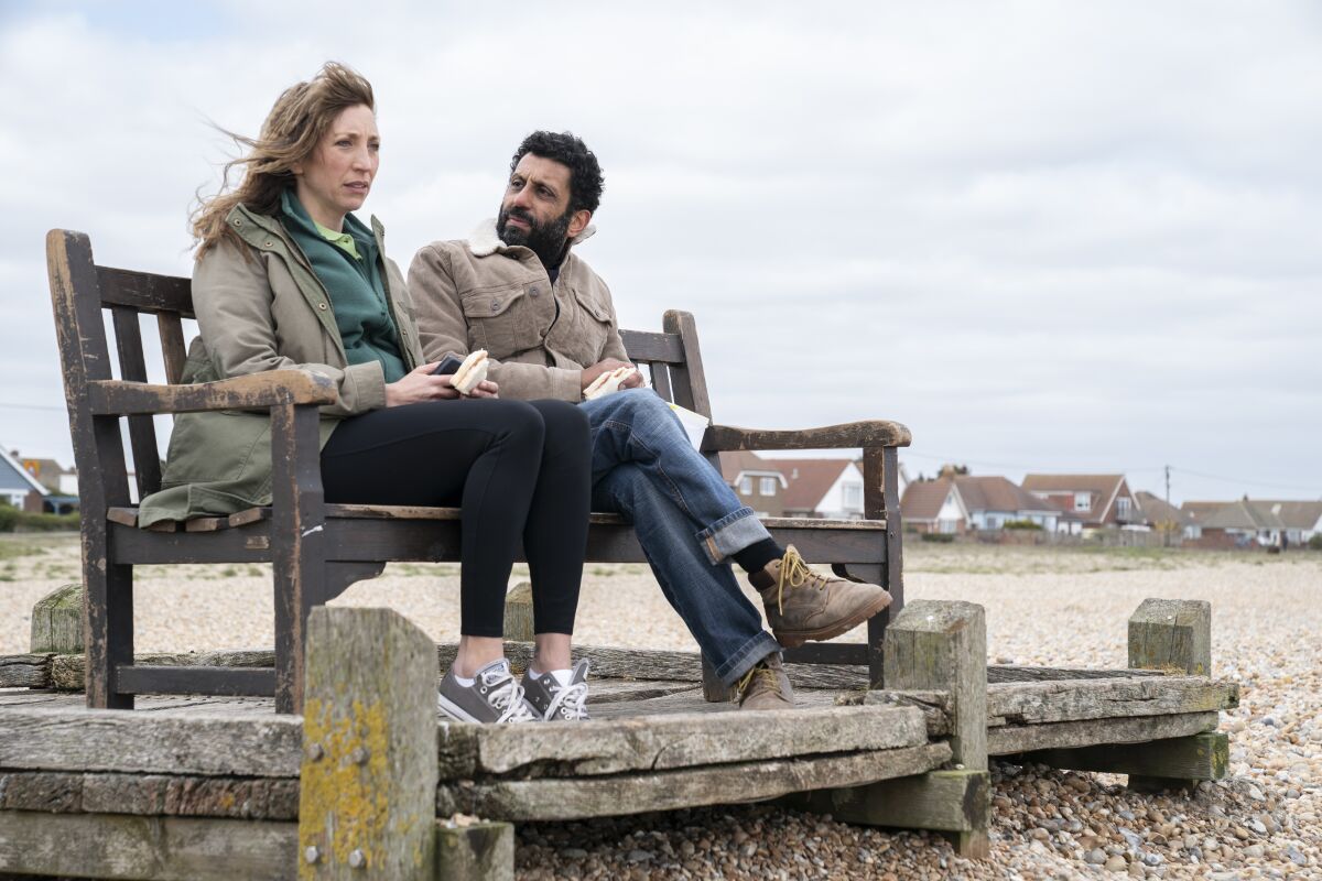A man and a woman sitting on a bench on the beach