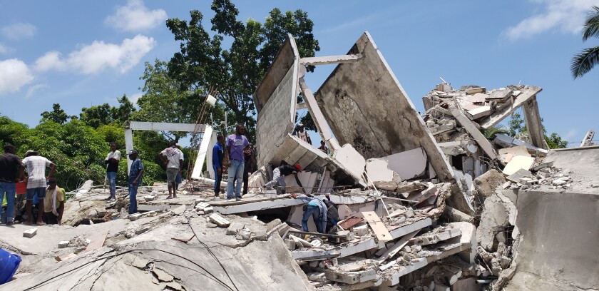 People walk over the remains of a building destroyed by an earthquake