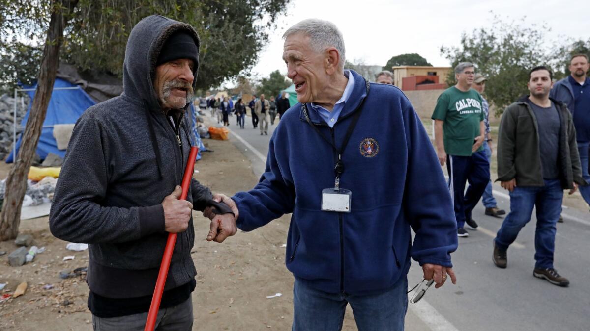 U.S. District Judge David Carter, right, greets Eddie S., 63, who is homeless, while surveying a homeless encampment along the Santa Ana River Trail in 2018. Carter is overseeing a lawsuit launched by homelessness advocates.