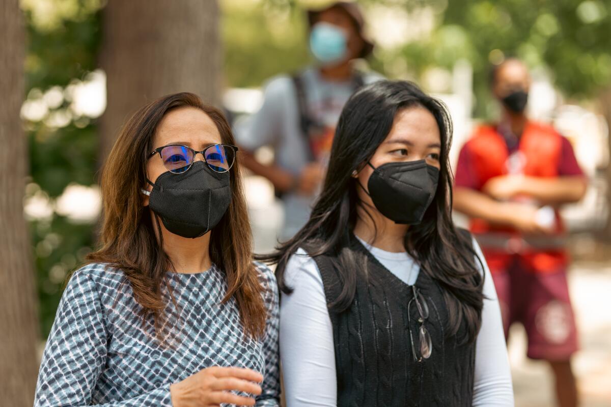 Two women wearing masks stand together.