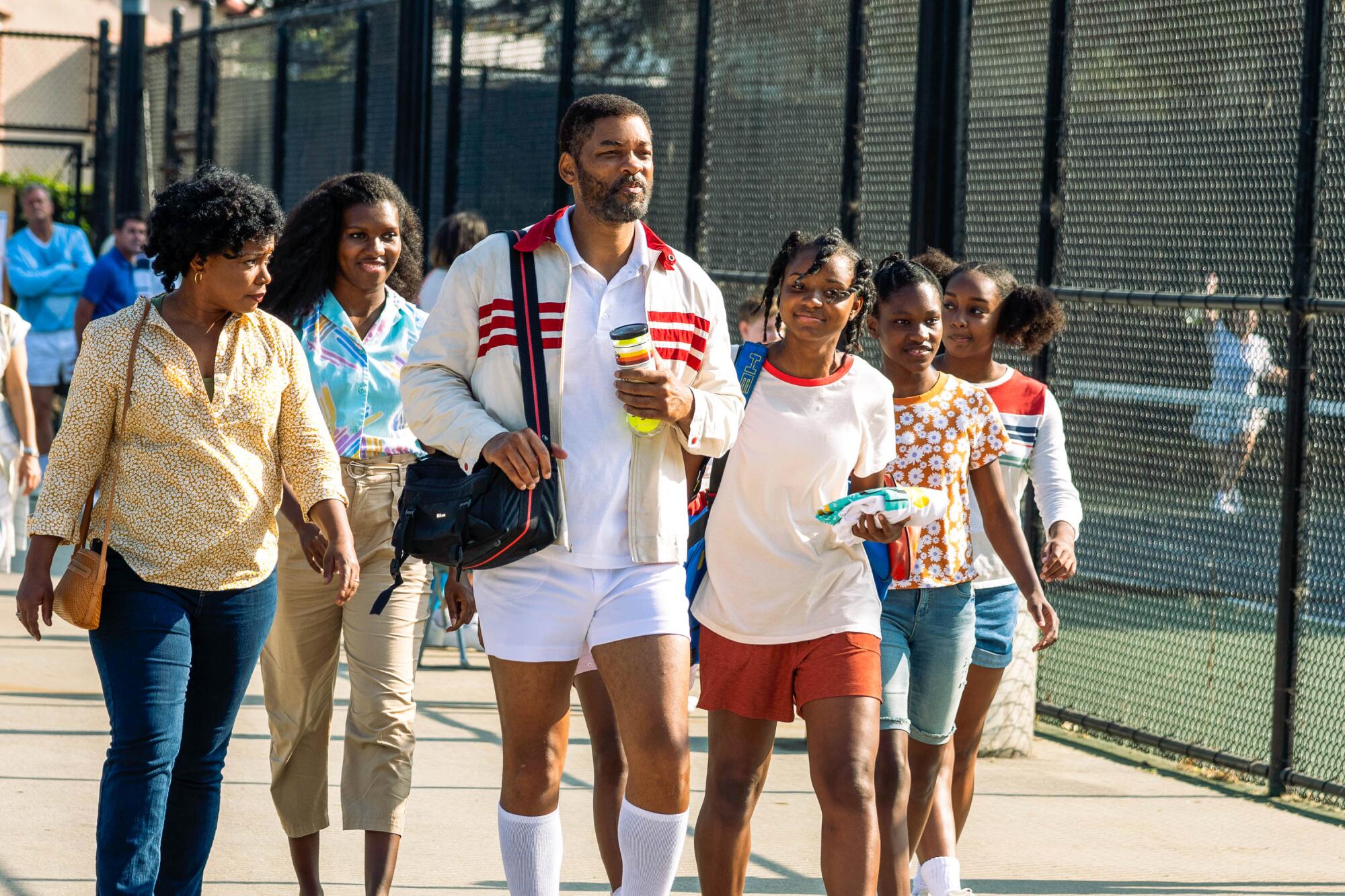 Aunjanue Ellis and Will Smith walk with their girls near tennis courts in a scene from "King Richard."