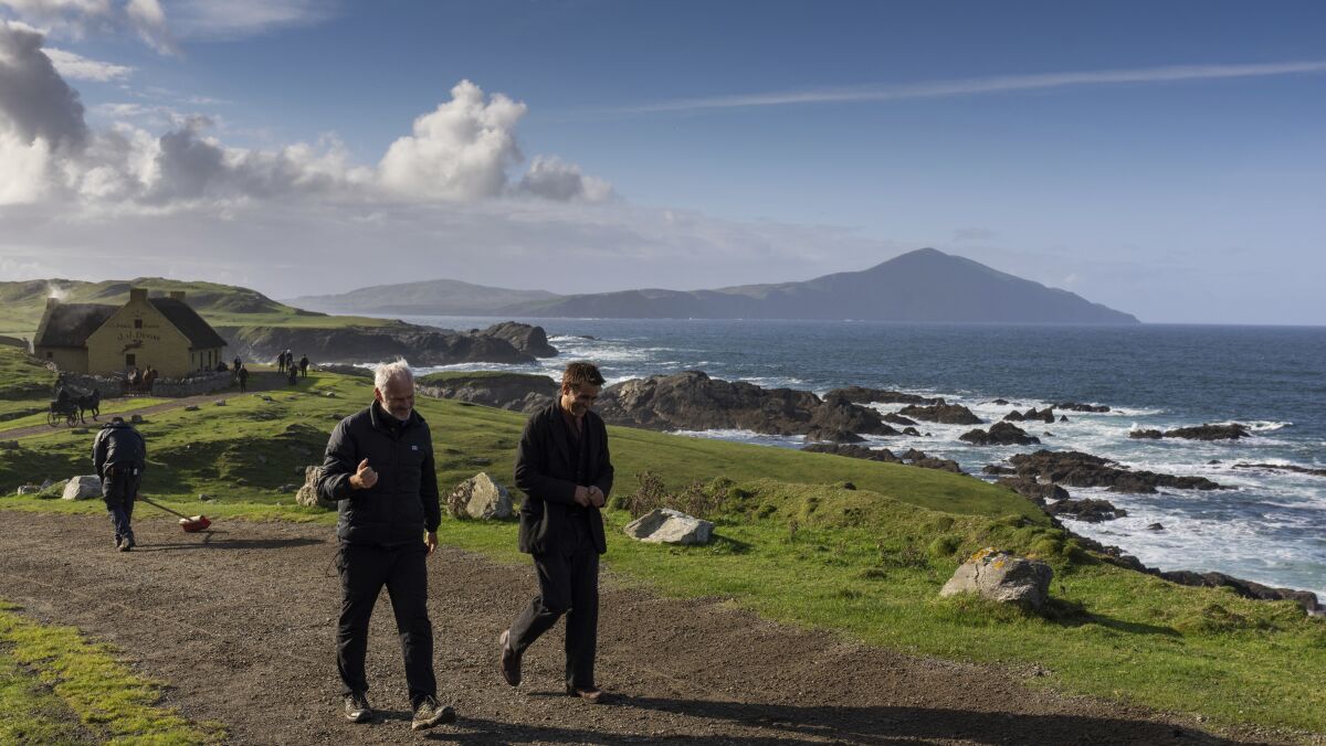 Two men walk on a dirt road overlooking the sea.