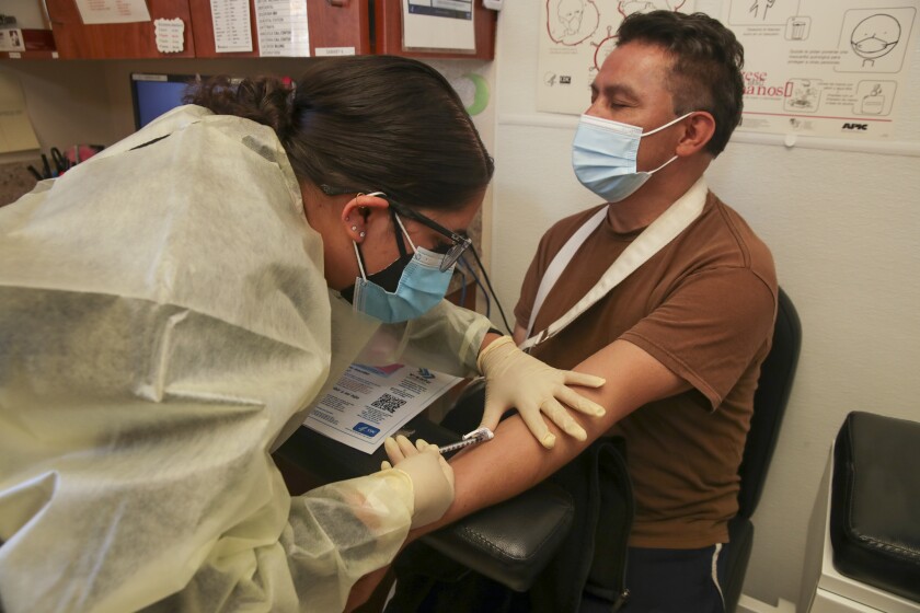 Bir kişinin sol koluna aşı enjekte eden bir sağlık çalışanı