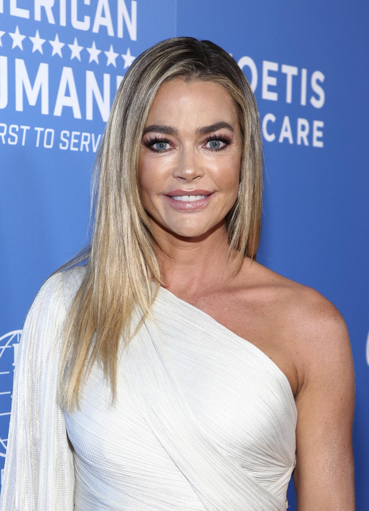 Denise Richards poses in a white dress at an event. 