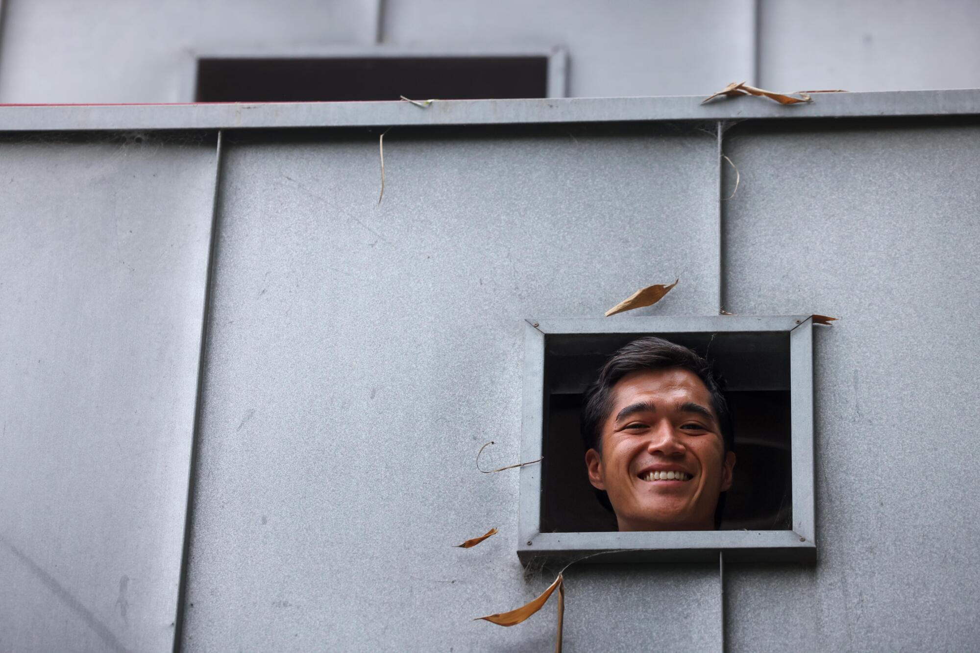 Owen Han's smiling face seen in a window in a gray wall