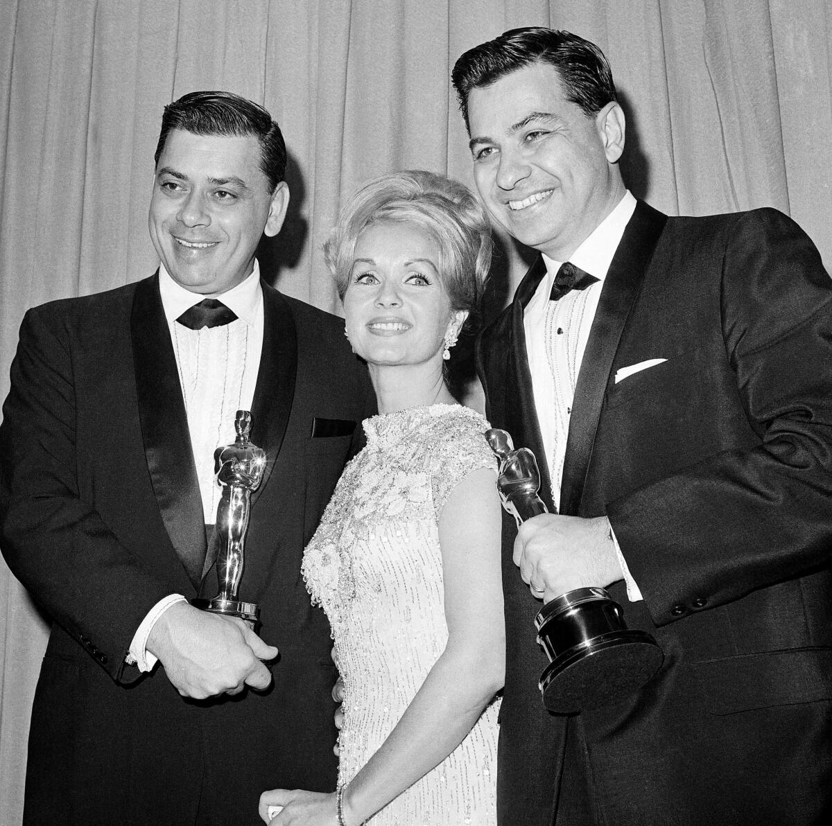 Debbie Reynolds stands between two men in tuxedoes holding Oscar statuettes