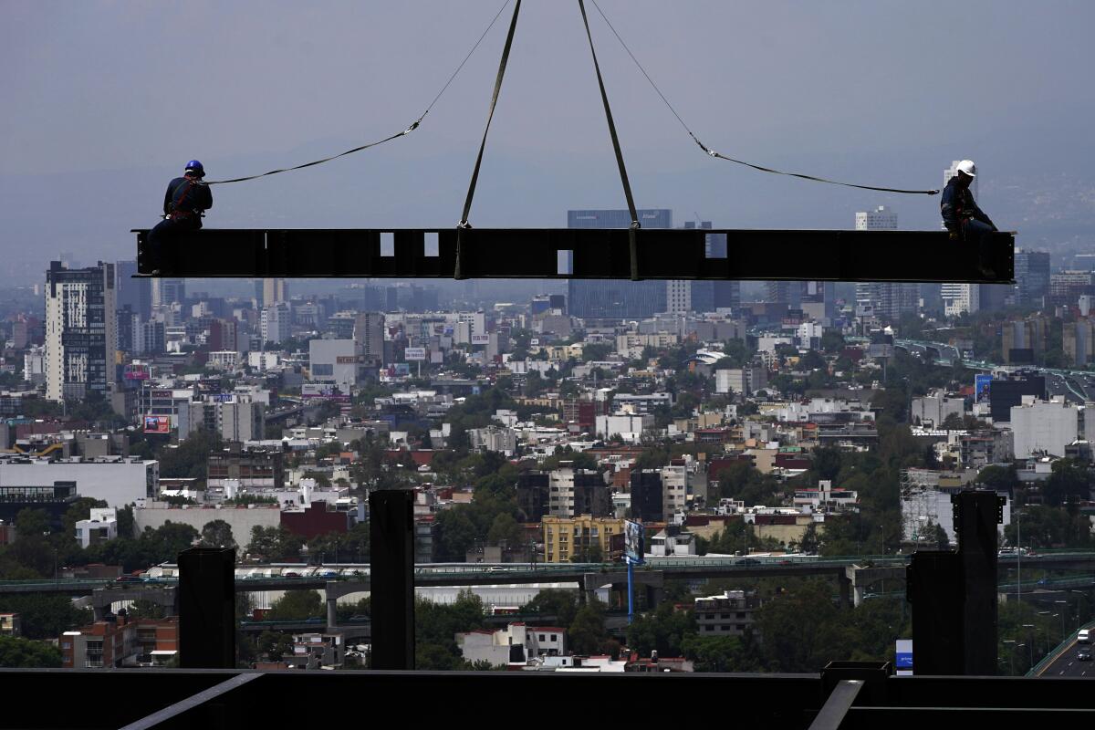 ARCHIVO - Trabajadores de la construcción están sobre una viga colgada de una grúa en un edificio 