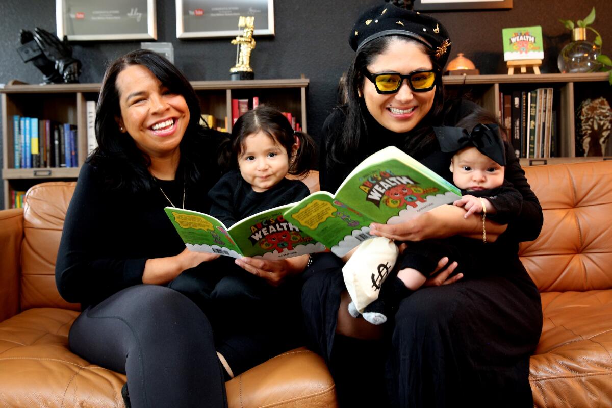 Two women smile while holding a baby and toddler at their home office.