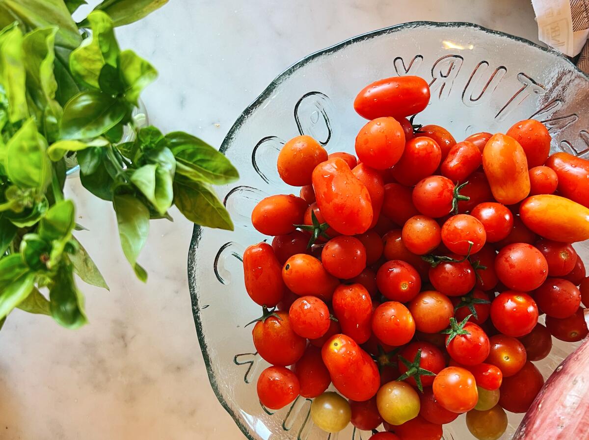 Small Datterini tomatoes in a glass bowl alongside a bunch of fresh basil